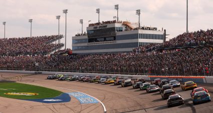 General view of packed stands at Iowa Speedway as cars come past the start-finish line.
